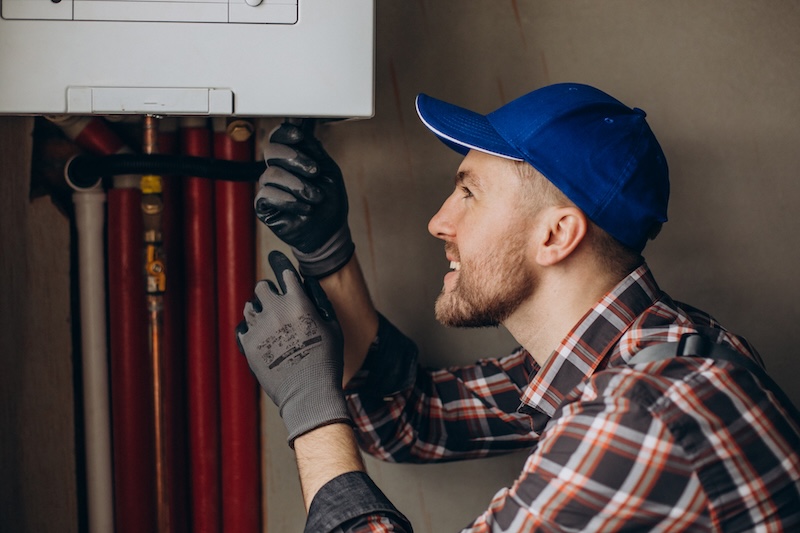Boiler engineer in cap and gloves working under a boiler